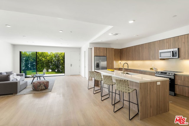 kitchen with a kitchen breakfast bar, stainless steel appliances, an island with sink, sink, and light hardwood / wood-style flooring