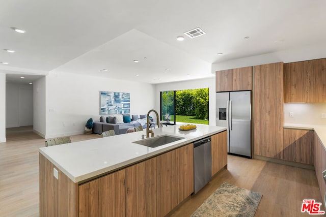 kitchen featuring stainless steel appliances, a center island with sink, sink, and light hardwood / wood-style flooring