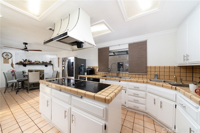 kitchen featuring sink, tasteful backsplash, white cabinetry, tile countertops, and a center island