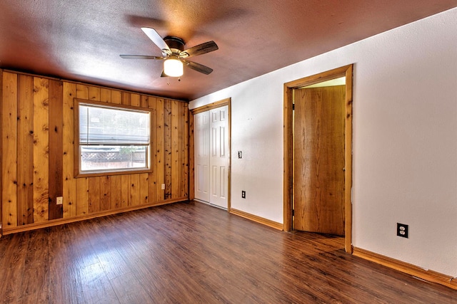 unfurnished bedroom featuring a textured ceiling, wooden walls, dark hardwood / wood-style flooring, and ceiling fan