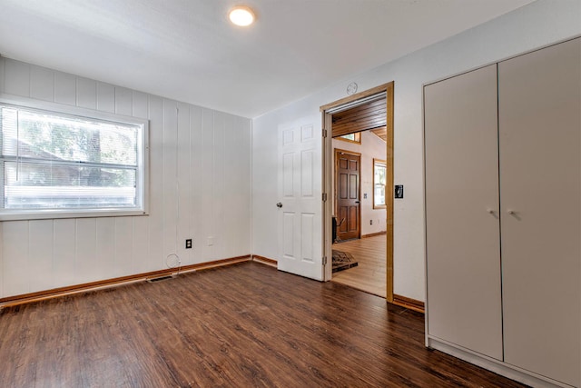 unfurnished bedroom with wooden walls, dark hardwood / wood-style flooring, and a closet