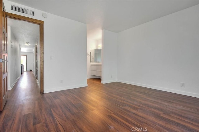 spare room with baseboards, visible vents, and dark wood-type flooring