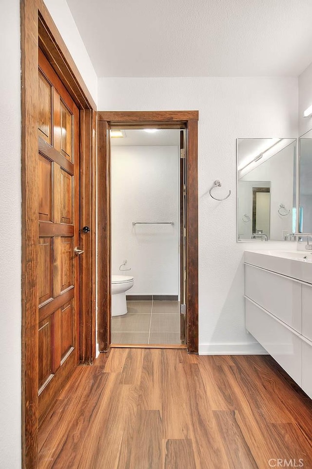 bathroom with toilet, wood finished floors, vanity, and baseboards