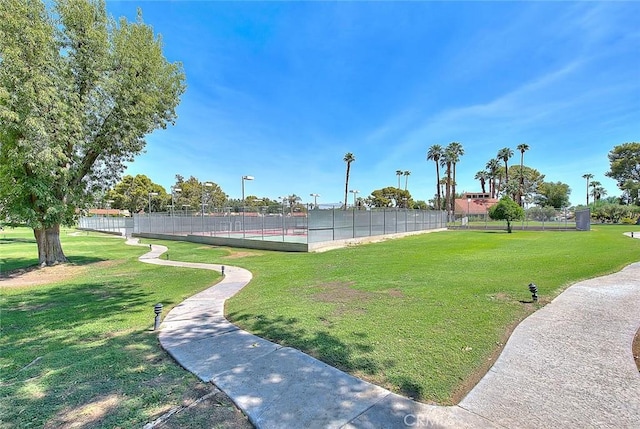 view of property's community with a tennis court, fence, and a yard