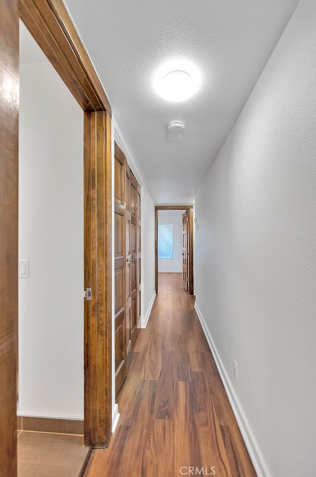 corridor with a textured ceiling and dark hardwood / wood-style flooring