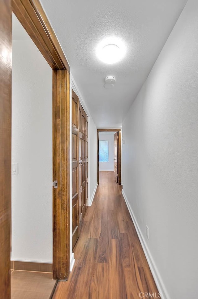hallway with a textured ceiling, dark wood finished floors, and baseboards