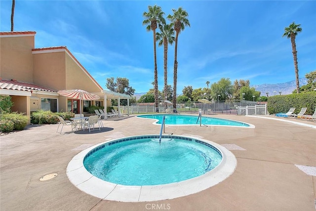 pool featuring fence, a patio area, a community hot tub, and a mountain view