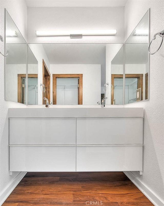 bathroom with baseboards, wood finished floors, a textured wall, and vanity