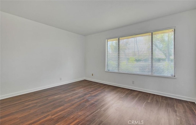 spare room featuring baseboards and dark wood finished floors