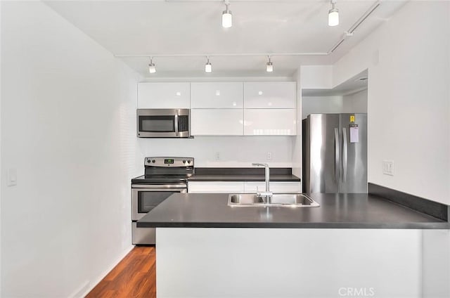 kitchen with appliances with stainless steel finishes, dark countertops, a sink, white cabinetry, and modern cabinets