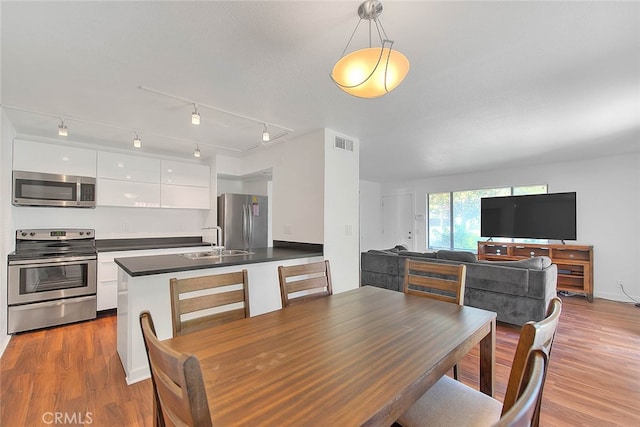 dining area with light hardwood / wood-style floors, sink, and rail lighting