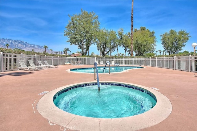 pool with a mountain view, a community hot tub, a patio area, and fence