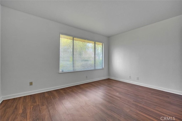 spare room with baseboards and dark wood-type flooring