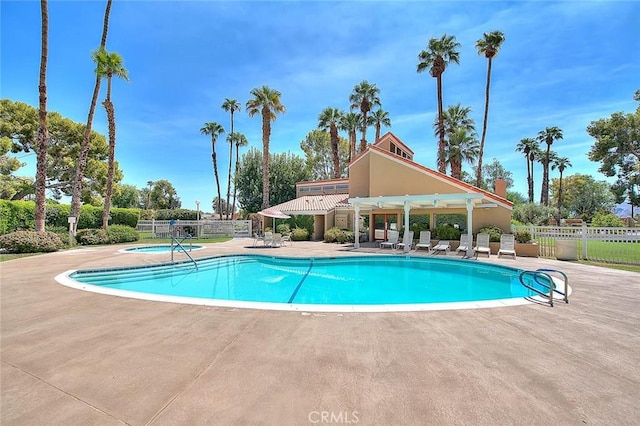 community pool with a patio, fence, and a hot tub