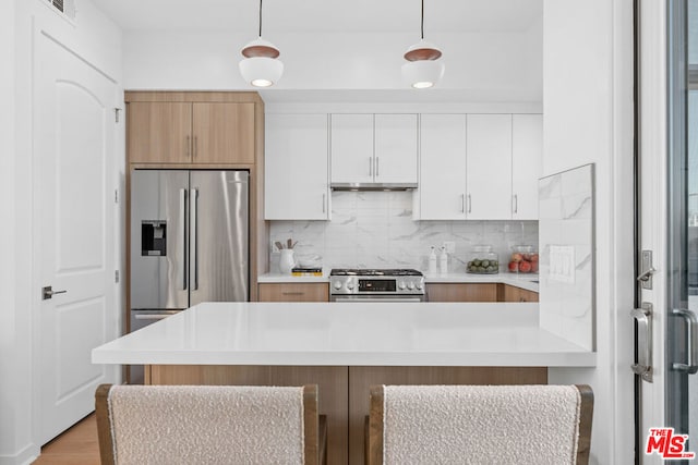 kitchen with light wood-type flooring, tasteful backsplash, white cabinets, hanging light fixtures, and appliances with stainless steel finishes