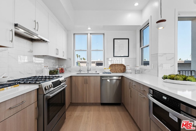 kitchen with sink, white cabinets, light hardwood / wood-style flooring, stainless steel appliances, and decorative backsplash