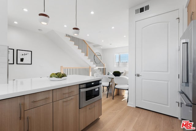 kitchen with stainless steel appliances, light hardwood / wood-style floors, and decorative light fixtures