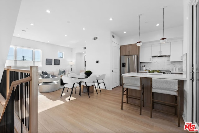 kitchen with white cabinets, pendant lighting, stainless steel fridge, light hardwood / wood-style flooring, and decorative backsplash