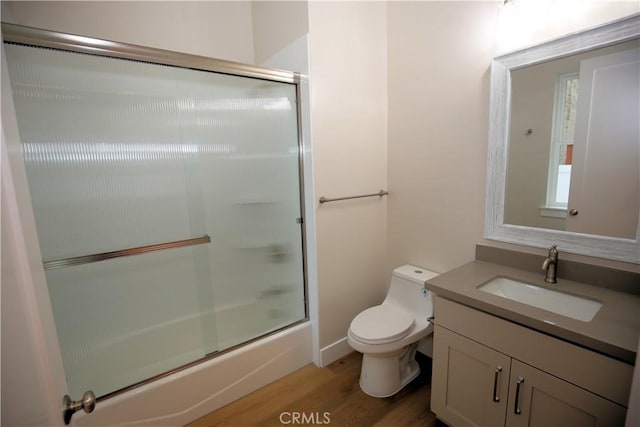 full bathroom featuring wood-type flooring, vanity, toilet, and bath / shower combo with glass door