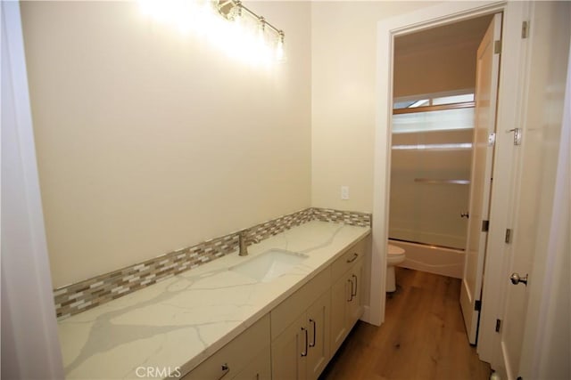 full bathroom with bath / shower combo with glass door, vanity, wood-type flooring, and toilet