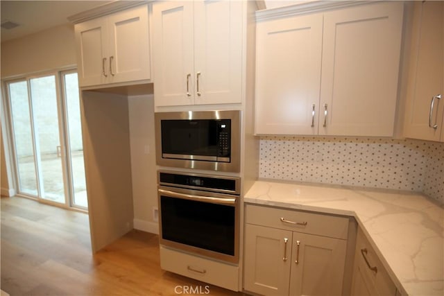 kitchen with white cabinets, light stone counters, appliances with stainless steel finishes, and light hardwood / wood-style flooring