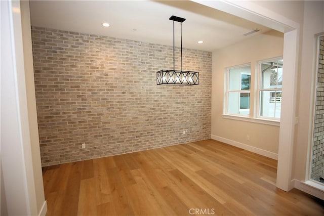 unfurnished dining area featuring brick wall and light wood-type flooring