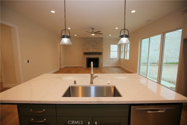 kitchen with light stone countertops, pendant lighting, stainless steel dishwasher, and sink