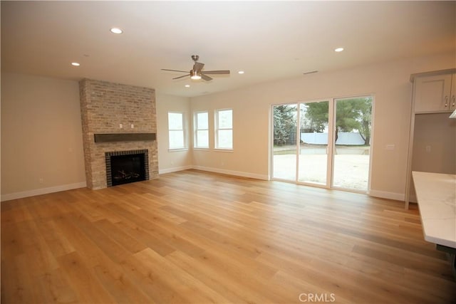 unfurnished living room featuring a fireplace, light wood-type flooring, and ceiling fan