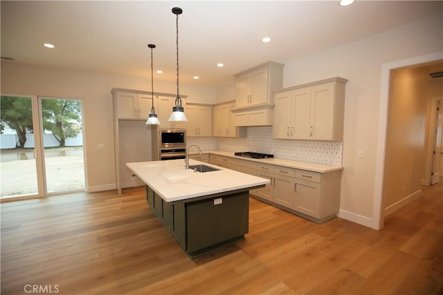 kitchen with appliances with stainless steel finishes, light wood-type flooring, sink, a center island with sink, and decorative light fixtures