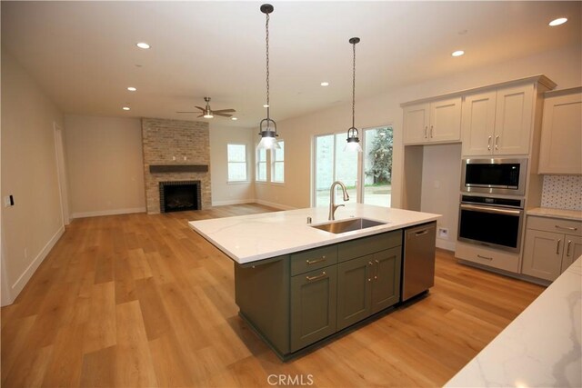 kitchen with sink, ceiling fan, light wood-type flooring, light stone counters, and stainless steel appliances