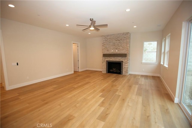 unfurnished living room with a brick fireplace, light hardwood / wood-style flooring, and ceiling fan