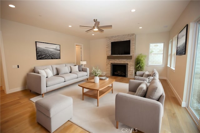 living room featuring ceiling fan, a fireplace, and light hardwood / wood-style flooring