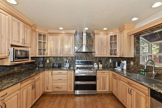 kitchen featuring wall chimney exhaust hood, dark stone countertops, sink, and appliances with stainless steel finishes