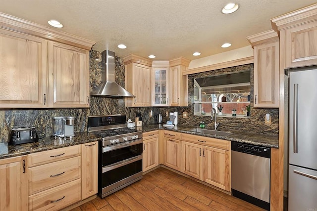 kitchen with wall chimney range hood, light hardwood / wood-style flooring, dark stone countertops, light brown cabinetry, and appliances with stainless steel finishes