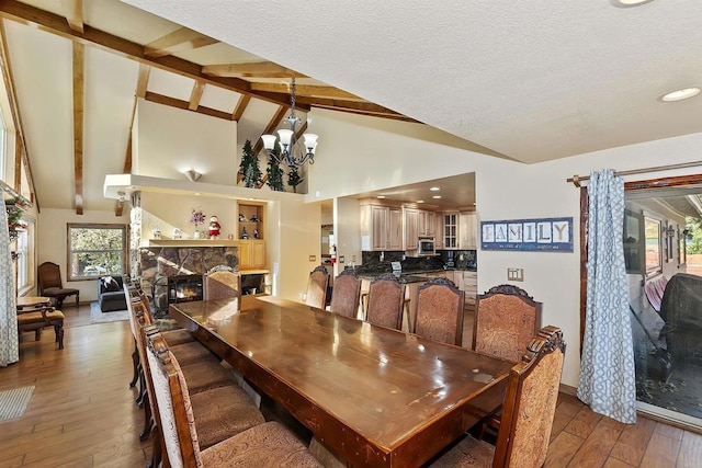 dining room with a chandelier, beam ceiling, light hardwood / wood-style flooring, and a stone fireplace