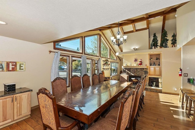 dining room with a chandelier, beam ceiling, hardwood / wood-style flooring, and a stone fireplace