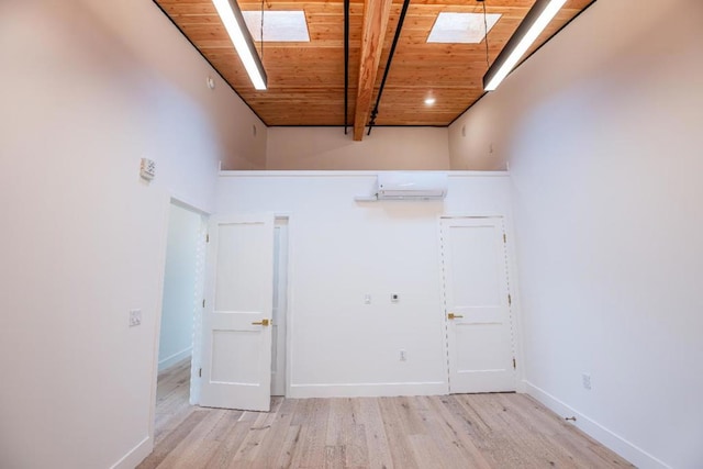 spare room featuring beamed ceiling, light wood-type flooring, wood ceiling, and a skylight