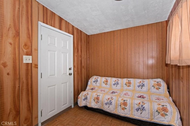 bedroom with wood walls, light parquet floors, and a textured ceiling