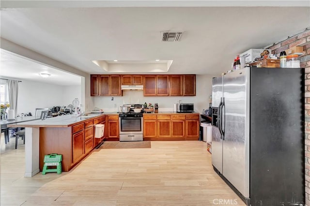 kitchen with stainless steel appliances, a raised ceiling, light hardwood / wood-style flooring, kitchen peninsula, and a breakfast bar