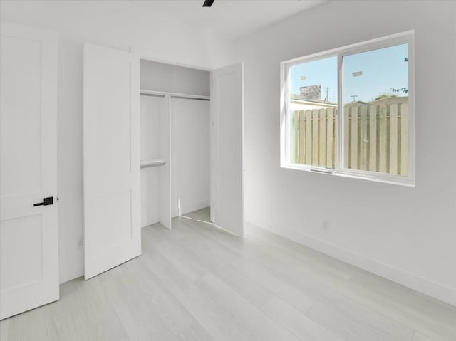 unfurnished bedroom with ceiling fan, a closet, multiple windows, and light hardwood / wood-style flooring