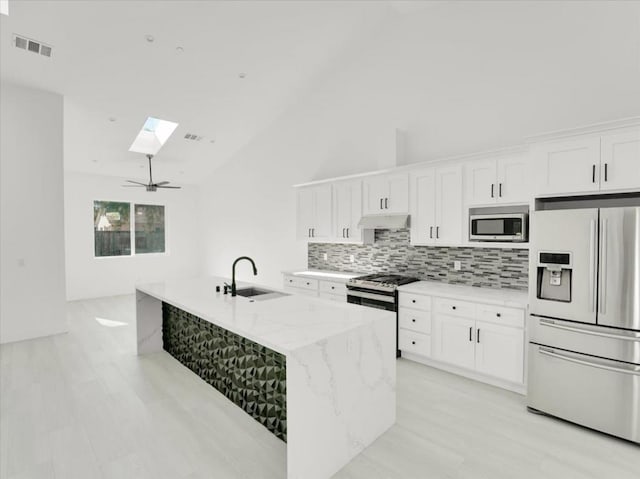 kitchen featuring white cabinetry, a skylight, light stone countertops, appliances with stainless steel finishes, and custom range hood