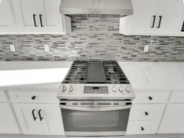 kitchen featuring stainless steel gas stove, wall chimney range hood, white cabinetry, and tasteful backsplash