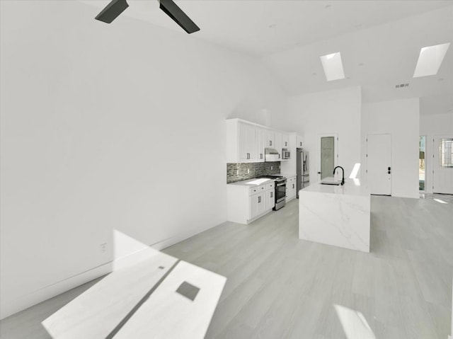 kitchen with white cabinets, a skylight, stainless steel appliances, tasteful backsplash, and light stone counters