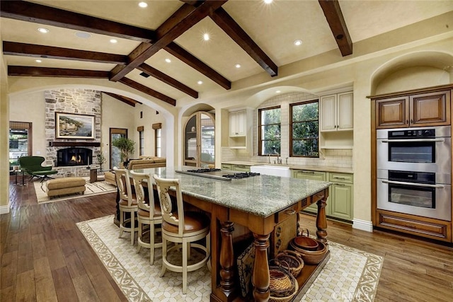 kitchen with appliances with stainless steel finishes, a center island, lofted ceiling with beams, light stone countertops, and a kitchen bar