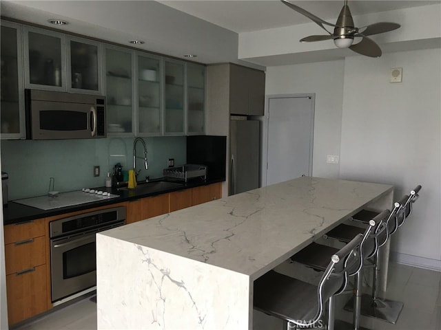 kitchen featuring a breakfast bar area, light stone countertops, sink, and appliances with stainless steel finishes