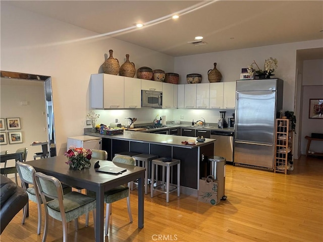 kitchen featuring white cabinets, stainless steel appliances, sink, light wood-type flooring, and a breakfast bar