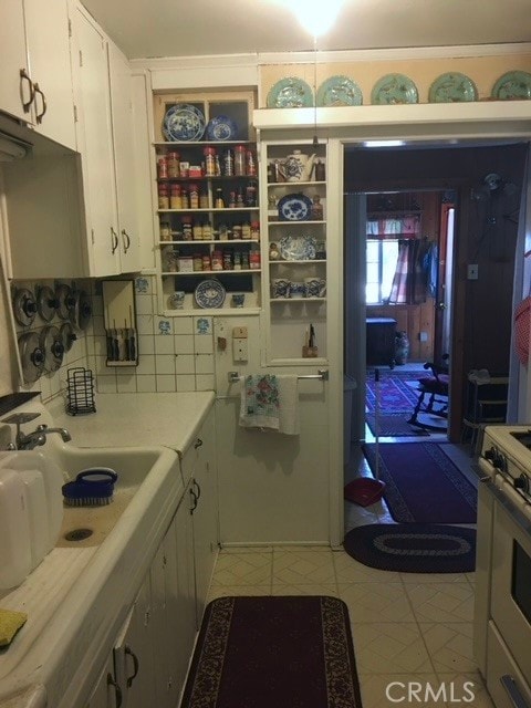 kitchen with white range with electric stovetop, light tile patterned floors, tasteful backsplash, and white cabinetry