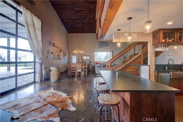 kitchen featuring a kitchen breakfast bar, an inviting chandelier, dishwasher, pendant lighting, and a towering ceiling