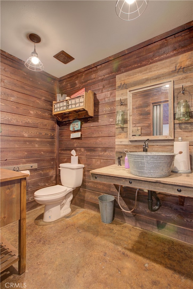 bathroom with toilet, wood walls, and sink