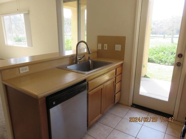 kitchen with a healthy amount of sunlight, stainless steel dishwasher, sink, and light tile patterned floors